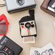 Handmade felt Polaroid Camera ornament from Craftspring, styled among vintage cameras and scattered Polaroid photographs—heirloom-quality decor that captures nostalgia and holiday cheer, ethically crafted by artisans in India using sustainable wool.