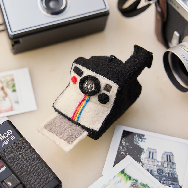 Handmade felt Polaroid Camera ornament from Craftspring, styled among vintage cameras and scattered Polaroid photographs—heirloom-quality decor that captures nostalgia and holiday cheer, ethically crafted by artisans in India using sustainable wool.