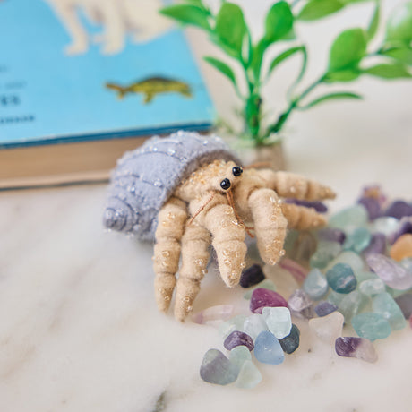 Handmade felt Hermit Crab ornament from Craftspring, featuring intricate beaded and embroidered details—displayed with aquarium rocks and a plant, perfect for ocean lovers, pet-themed decor, and whimsical holiday gifting, ethically crafted by artisans using sustainable wool.