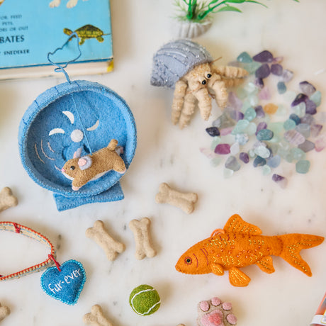 Craftspring’s handmade felt Hamster on a Wheel, Goldfish, and Hermit Crab Christmas ornaments displayed together among pet supplies—featuring charming embroidered details, perfect for whimsical holiday gifting, ethically crafted by artisans using sustainable wool.