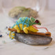 Craftspring’s handmade felt Chameleon Christmas ornament displayed on a rock—featuring beaded details, a curled tail, and a long tongue catching a bug, perfect for fun and unique holiday gifting, ethically crafted by artisans using sustainable wool.