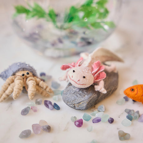 Craftspring’s handmade felt Axolotl and Hermit Crab Christmas ornaments displayed among aquarium stones with a fish bowl—featuring intricate embroidered and beaded details, perfect for playful holiday gifting, ethically crafted by artisans using sustainable wool.