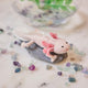 Craftspring’s handmade felt Axolotl Christmas ornament displayed among aquarium stones—featuring a cute pink design with intricate embroidered and beaded details, perfect for whimsical holiday gifting, ethically crafted by artisans using sustainable wool.