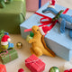 Handmade felt Orange T-Rex Dinoclaus ornament from Craftspring, displayed among wrapped presents and bobble ornaments alongside other Santa dinosaur ornaments—perfect for dino-loving kids and playful holiday gifting, ethically crafted by artisans using sustainable wool.