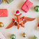 Handmade felt Merry Pterodactyl ornament from Craftspring on marble with bobbles and mini presents—wearing a Santa hat and holding a “MERRY” garland, perfect for dino-loving kids and festive holiday gifting, ethically crafted using sustainable wool.