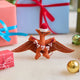Handmade felt Merry Pterodactyl ornament from Craftspring, displayed in front of festive wrapped presents—perfect for dino-loving kids and joyful holiday gifting, featuring embroidered details, a red Santa hat, and a “MERRY” garland, ethically crafted using sustainable wool.