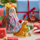 Handmade felt Orange T-Rex Dinoclaus ornament from Craftspring, displayed in front of a volcano school project and surrounded by wrapped presents—perfect for dino-loving kids and playful holiday gifting, ethically crafted by artisans using sustainable wool.