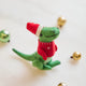 Handmade felt Santasaurus T-Rex ornament from Craftspring, displayed on marble with festive bobble ornaments—featuring a red Santa hat, red sweater, and embroidered details, perfect for dino-loving kids and cheerful holiday gifting, ethically crafted using sustainable wool.