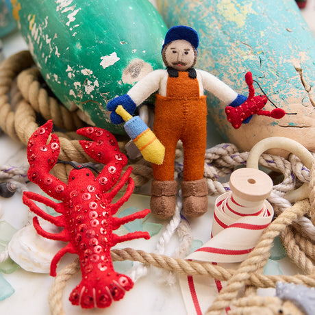 Lifestyle photo of Craftspring’s handmade felt Maine Lobsterman and Bejeweled Red Lobster Christmas ornaments, featuring intricate beaded and embroidered details—displayed with nautical ropes and buoys for a whimsical coastal holiday scene. Ethically crafted by artisans using sustainable wool.