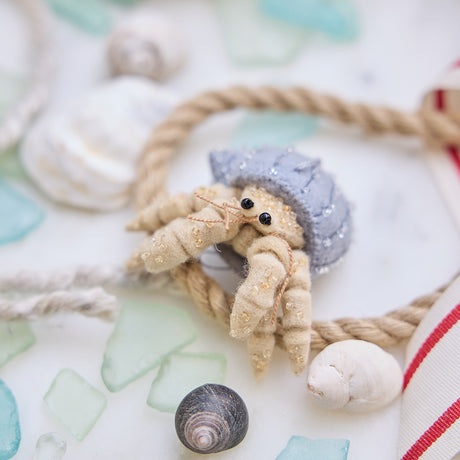 Handmade felt Hermit Crab ornament from Craftspring, with intricate beaded and embroidered details—displayed with sea glass, rope, and shells, perfect for ocean lovers and whimsical holiday gifting, sustainably handmade by artisans.