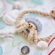Handmade felt Hermit Crab ornament from Craftspring, with intricate beaded and embroidered details—displayed with sea glass, rope, and shells, perfect for ocean lovers and whimsical holiday gifting, sustainably handmade by artisans.