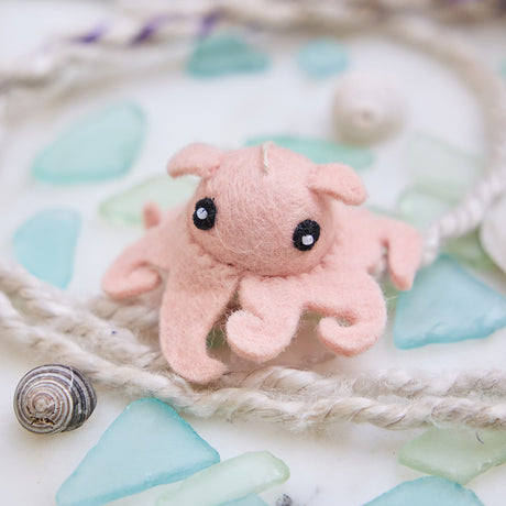 Handmade felt Dumbo Octopus ornament from Craftspring, featuring adorable curly pink tentacles and charming embroidered details—cuddled among sea glass, rope, and shells for a sweet coastal Christmas vibe, lovingly crafted by artisans using sustainable wool.