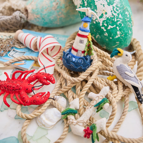 Handmade felt Anchor, Seagull, Holiday Lighthouse, and Lobster ornaments from Craftspring, featuring detailed embroidery, appliqué, and beaded accents—displayed with rope and lobster buoys, perfect for nautical holiday decor and gifting, sustainably handmade by artisans using wool.