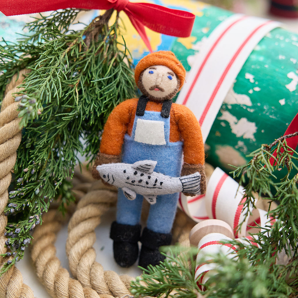 Handmade felt Old Man Salmon ornament from Craftspring, featuring a fisherman in a blue bib holding a silver salmon—displayed among nautical Christmas decor, heirloom-quality holiday decor with embroidered details, ethically handmade by artisans using sustainable wool.