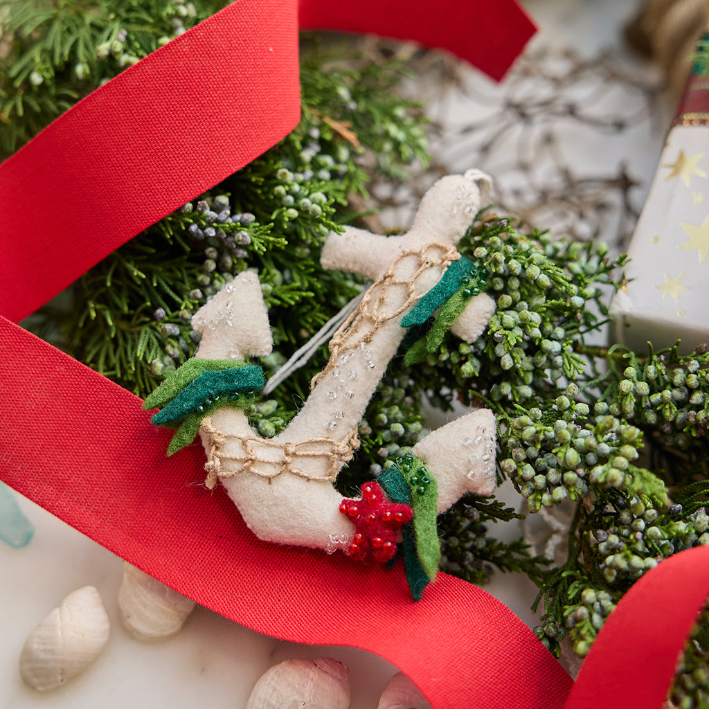 Handmade felt Anchor Christmas ornament from Craftspring, featuring beaded barnacles, appliqué seaweed and starfish, and draped in netting—displayed on evergreens with a red ribbon, perfect for nautical holiday decor and gifting, sustainably handmade by artisans using wool.