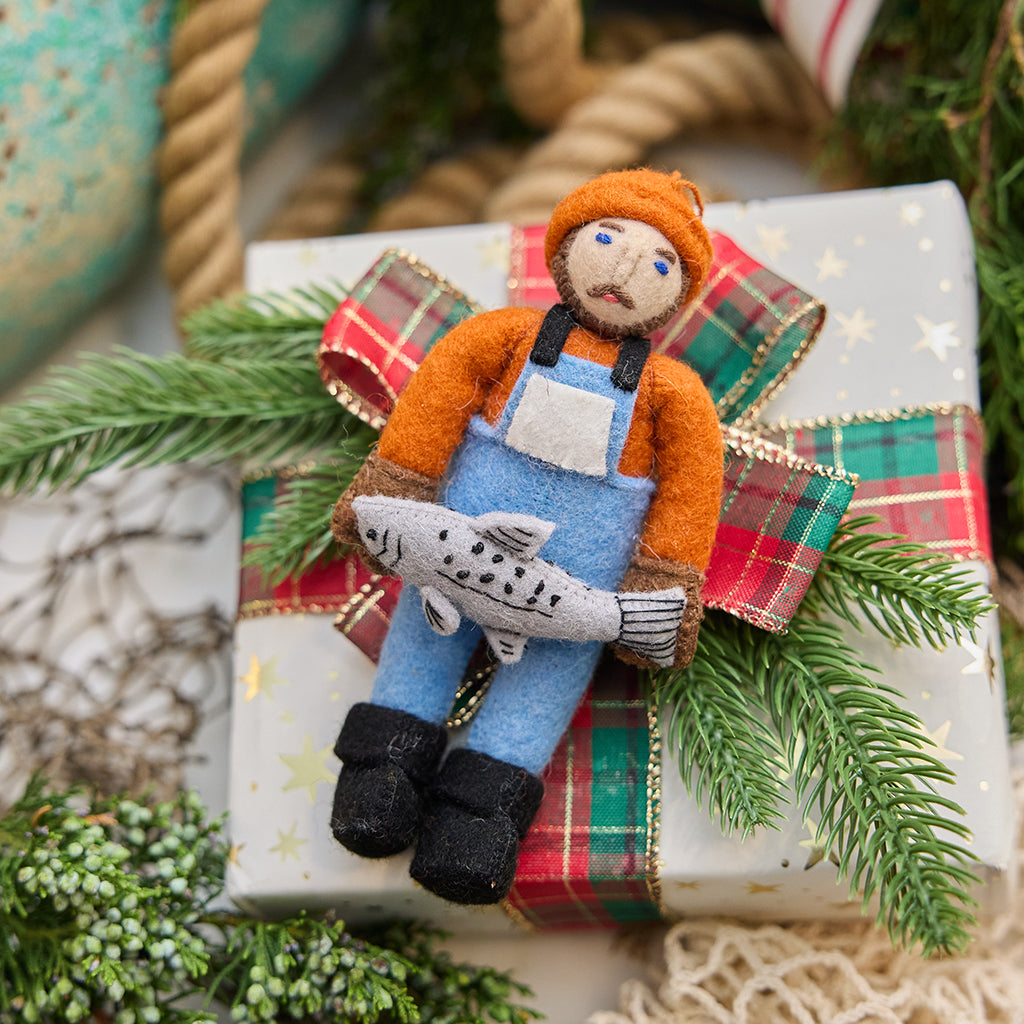 Handmade felt Old Man Salmon ornament from Craftspring, featuring a fisherman in a blue bib holding a silver salmon—displayed on a holiday gift, heirloom-quality Christmas decor with embroidered details, ethically handmade by artisans using sustainable wool.