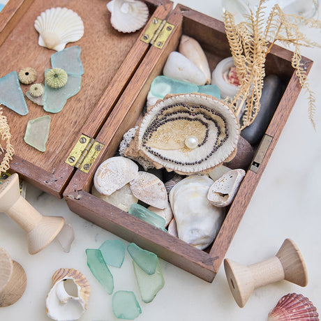 Lifestyle photo of Craftspring’s handmade felt Oyster Christmas ornament, nestled in a wooden box filled with shells and sea glass—featuring a beaded pearl and shimmering embroidered details, ethically crafted by artisans using sustainable wool for ocean-inspired holiday charm.









