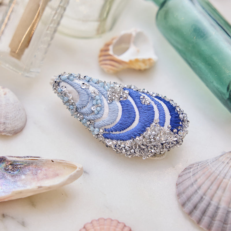 Craftspring’s Mussel Shell Ornament displayed among seashells and glass bottles — highlighting its intricate beaded and embroidered details, creating a festive and coastal holiday scene, ethically crafted by artisans.