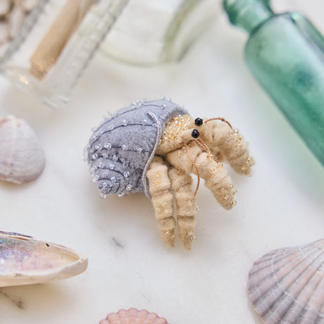 Handmade felt Hermit Crab ornament from Craftspring, with intricate beaded and embroidered details—displayed with sea glass and shells, perfect for ocean lovers and whimsical holiday gifting, sustainably handmade by artisans.