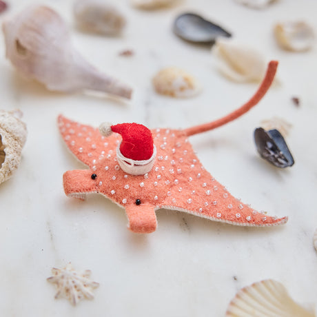 Handmade felt Santa Coral Manta ornament from Craftspring, featuring intricate beaded and embroidered details and a festive Santa hat—displayed among shells for a whimsical coastal Christmas scene, ethically crafted by artisans using sustainable wool.