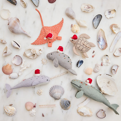 Craftspring’s handmade felt ocean animal Christmas ornaments—featuring the Spyhop Gray Whale, Sea Turtle, Manta Ray, Manatee, and Narwhal—each wearing a red Santa hat and displayed among seashells, with intricate embroidered details perfect for festive coastal holiday gifting, ethically crafted by artisans using sustainable wool.