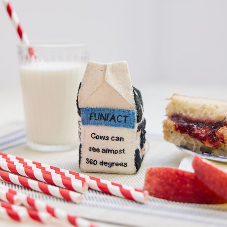 Lifestyle photo of Craftspring’s handmade felt School Milk Carton ornament, featuring embroidered and appliqué details—displayed with a PB&J sandwich, apple slices, and a glass of milk, perfect for nostalgic holiday gifting and lovingly crafted by artisans using sustainable wool.