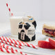 Lifestyle photo of Craftspring’s handmade felt School Milk Carton ornament, featuring embroidered and appliqué details—displayed with a PB&J sandwich, apple slices, and a glass of milk, perfect for nostalgic holiday gifting and lovingly crafted by artisans using sustainable wool.