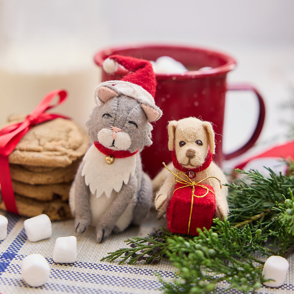 Handmade felt Dog with Gift and Santa Cat ornaments from Craftspring—displayed with a mug of hot cocoa and cookies, perfect for festive pet lovers and cozy holiday gifting, ethically crafted by artisans using sustainable wool.