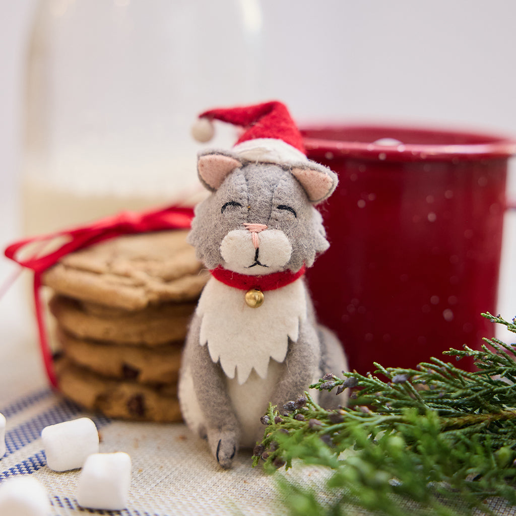 Handmade felt Santa Cat ornament from Craftspring, featuring a gray cat wearing a red Santa hat—displayed with a mug of hot cocoa and cookies, perfect for festive cat lovers and cozy holiday gifting, ethically crafted by artisans using sustainable wool.