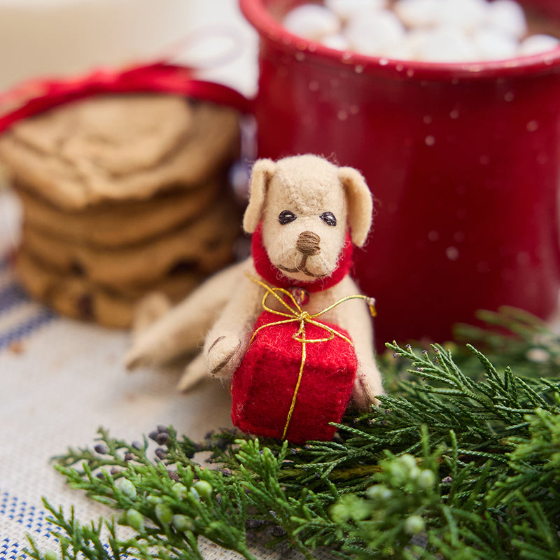 Handmade felt Dog with Gift ornament from Craftspring, featuring a pup holding a red present between its paws—displayed with a mug of hot cocoa and cookies, perfect for festive dog lovers and cozy holiday gifting, ethically crafted by artisans using sustainable wool.