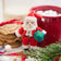 Handmade felt Sweet Little Santa ornament from Craftspring, featuring an adorable Santa with rosy cheeks and a cute round nose holding a gift—displayed with hot cocoa, cookies, and evergreen branches, perfect for cozy Christmas moments and festive gifting, ethically crafted by artisans using sustainable wool.