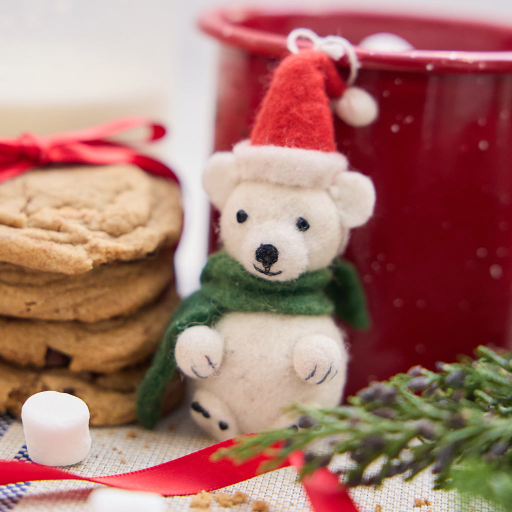 Handmade felt Little Drop Polar Bear ornament from Craftspring, featuring a polar bear wearing a Santa hat and green scarf—displayed with hot cocoa, cookies, and evergreen branches, perfect for cozy Christmas moments and festive gifting, ethically crafted by artisans using sustainable wool.