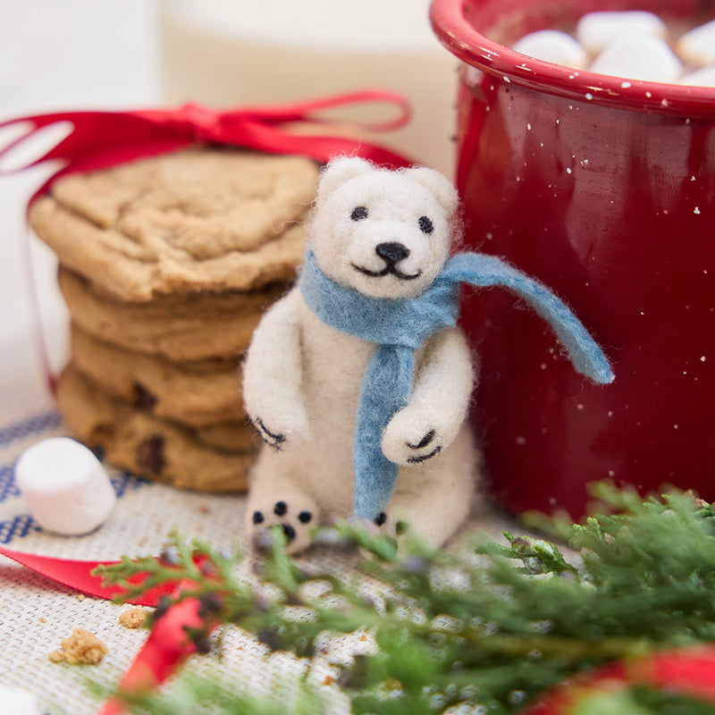 Handmade needle-felted Chilly Polar Bear ornament from Craftspring, featuring a white polar bear wearing a cozy blue scarf—displayed with hot cocoa, cookies, and evergreen branches, perfect for cozy Christmas moments and festive gifting, ethically crafted by artisans using sustainable wool.