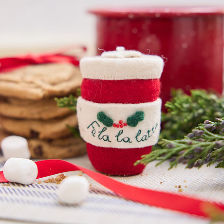 Handmade felt Fa La La Latte ornament from Craftspring, featuring a red to-go cup with “Fa la la latte” and holly on one side, a Christmas tree on the other, and a heart-shaped latte foam on top—displayed with hot cocoa and cookies, perfect for cozy Christmas cheer and festive gifting, ethically crafted by artisans using sustainable wool.
