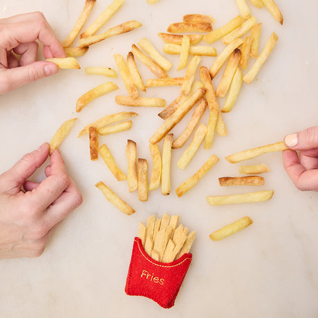 Lifestyle photo of Craftspring’s French Fries ornament, surrounded by real French fries with hands reaching in—playful holiday decor for food lovers, ethically handmade by artisans using sustainable wool.