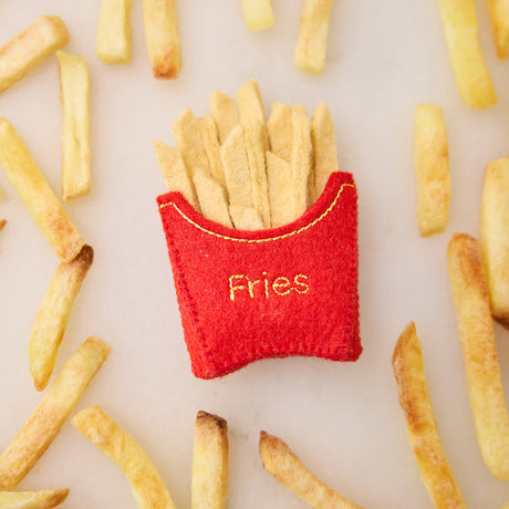 Lifestyle photo of Craftspring’s French Fries ornament, featuring golden felt fries with playful embroidered details—displayed on a marble surface surrounded by real French fries, perfect for food lovers and whimsical holiday gifting, ethically handmade by artisans using sustainable wool.
