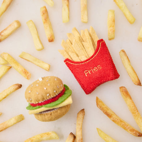 Lifestyle photo of Craftspring’s French Fries and NY’s Best Cheeseburger ornaments, displayed among real fries on marble—festive felt food fun for holiday gifting, ethically handmade by artisans using sustainable wool.