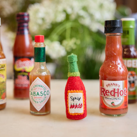 Handmade felt Hot Sauce ornament from Craftspring, featuring bold embroidered details—displayed among real hot sauce bottles, perfect for spicy food lovers and unique holiday gifting, sustainably handmade by artisans using wool.