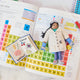 Craftspring’s handmade felt STEAM Book and Young Scientist Christmas ornaments displayed together on a science textbook—featuring intricate beaded and embroidered details that celebrate curiosity and learning, ethically crafted by artisans using sustainable wool.