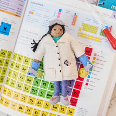 Craftspring’s handmade felt Young Scientist Christmas ornament displayed on a science textbook—featuring intricate beaded and embroidered details that celebrate curiosity and discovery, ethically crafted by artisans using sustainable wool.