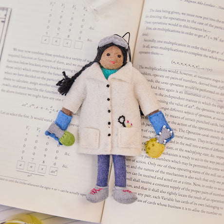 Craftspring’s handmade felt Young Scientist Christmas ornament displayed on an open science book—perfect for thoughtful holiday gifting, showcasing intricate beaded and embroidered details that inspire curiosity and learning, ethically crafted by artisans using sustainable wool.