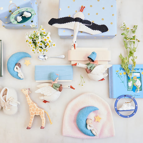 Handmade felt ornaments from Craftspring’s New Baby collection, featuring a baby sleeping on the moon, babies riding flying geese, and a stork—available in both brown and light skin tones—perfect for charming nursery decor and heartfelt baby shower gifts, ethically crafted using sustainable wool.