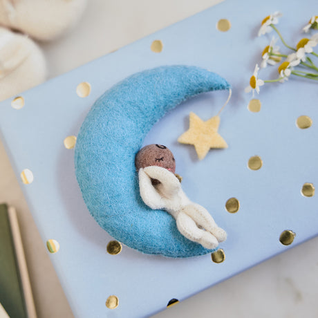 Handmade felt Moon Dreamer Baby Ornament – Brown from Craftspring, featuring a sleeping baby with brown skin on a crescent moon with a dangling star—displayed on a wrapped gift, perfect for nursery decor and thoughtful baby shower gifting, ethically crafted by artisans using sustainable wool.
