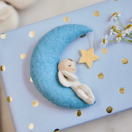 Handmade felt Moon Dreamer Baby Ornament – Light from Craftspring, displayed on a wrapped gift—featuring a sleeping baby with light skin on a crescent moon with a dangling star, perfect for nursery decor and thoughtful baby shower gifting, ethically crafted using sustainable wool.