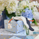 Handmade felt New Baby Stork ornament from Craftspring, featuring a stork carrying a bundle with delicate beaded and embroidered details—displayed hanging in front of flowers and presents, perfect for nursery decor and thoughtful baby shower gifting, ethically crafted by artisans using sustainable wool.