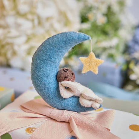 Handmade felt Moon Dreamer Baby Ornament – Brown from Craftspring, featuring a sleeping baby with brown skin on a crescent moon with a dangling star—displayed on a wrapped gift, perfect for nursery decor and thoughtful baby shower gifting, ethically crafted by artisans using sustainable wool.