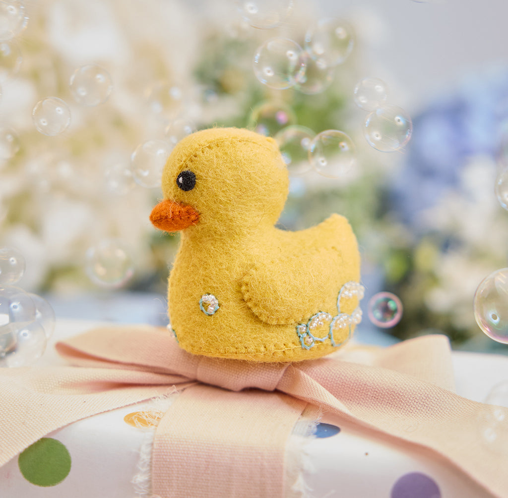 Handmade felt Rubber Duck ornament from Craftspring, featuring embroidered and beaded soap bubbles—displayed on a wrapped gift surrounded by bubbles, perfect for nursery decor and thoughtful baby shower gifting, ethically crafted by artisans using sustainable wool.