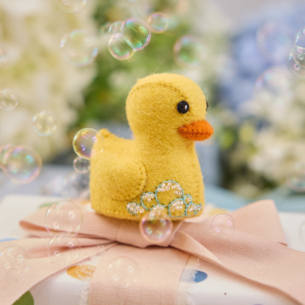 Handmade felt Rubber Duck ornament from Craftspring, featuring embroidered and beaded soap bubbles—displayed on a wrapped gift surrounded by bubbles, perfect for nursery decor and thoughtful baby shower gifting, ethically crafted by artisans using sustainable wool.