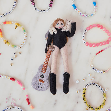 Craftspring’s handmade felt Taylor Swift with Cat Christmas ornament displayed surrounded by friendship bracelets—featuring Taylor holding a guitar with the number 13 and a cat around her shoulders, perfect for Swiftie holiday gifting, ethically crafted by artisans using sustainable wool.