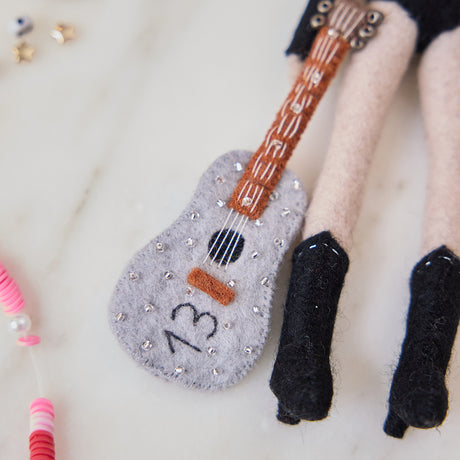 Craftspring’s handmade felt Taylor Swift with Cat Christmas ornament displayed surrounded by friendship bracelets—featuring Taylor holding a guitar with the number 13 and a cat around her shoulders, perfect for Swiftie holiday gifting, ethically crafted by artisans using sustainable wool.